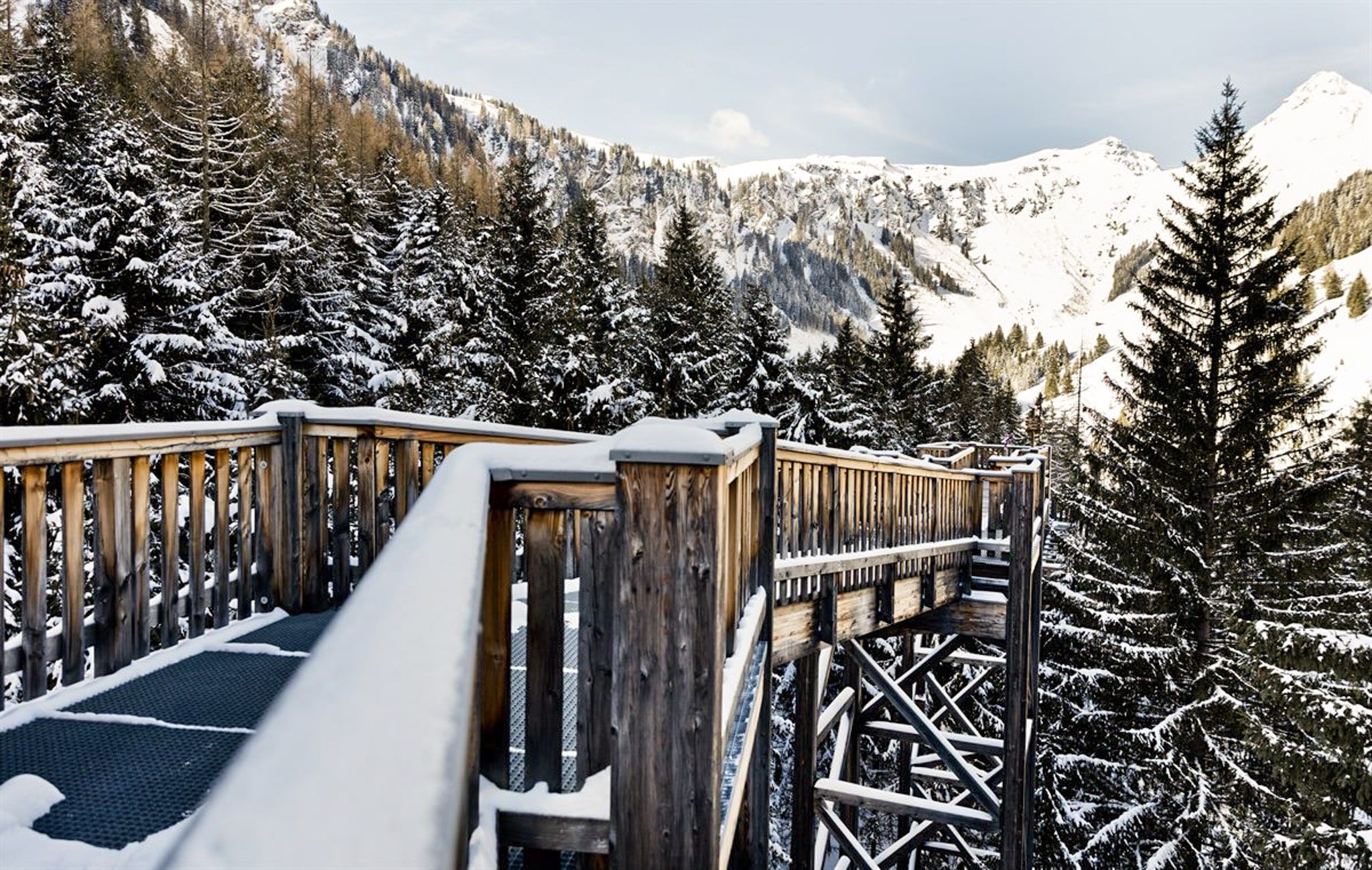 A wooden walkway leads through snowy trees in the Glemmtal.