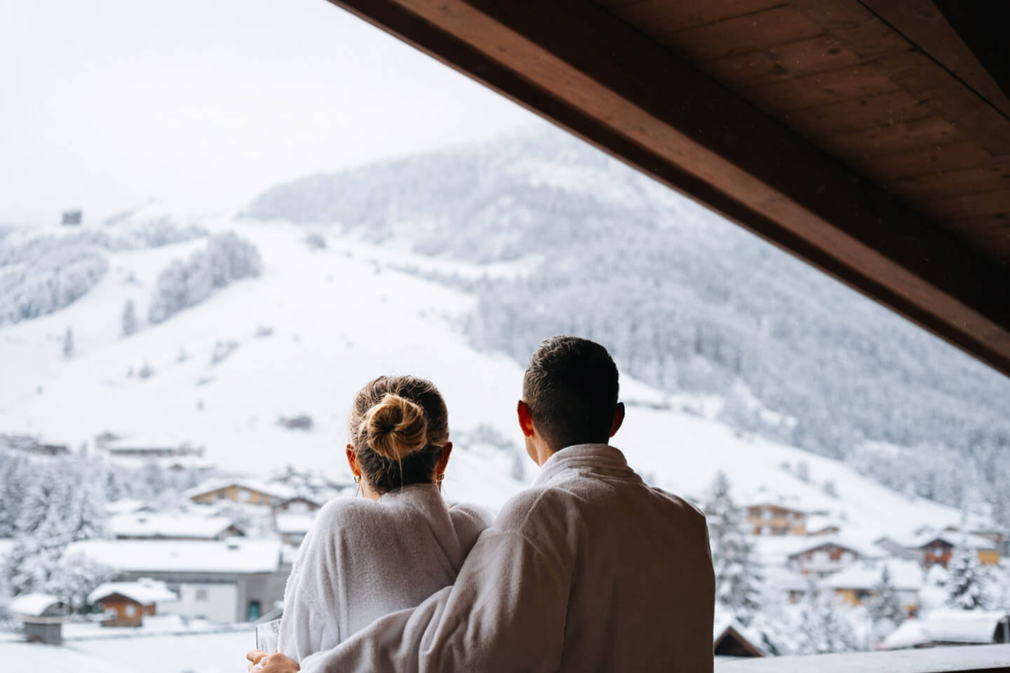 Paar im Bademantel schaut auf die verschneite Glemmtal Landschaft vom Glemmtalerhof in Hinterglemm.
