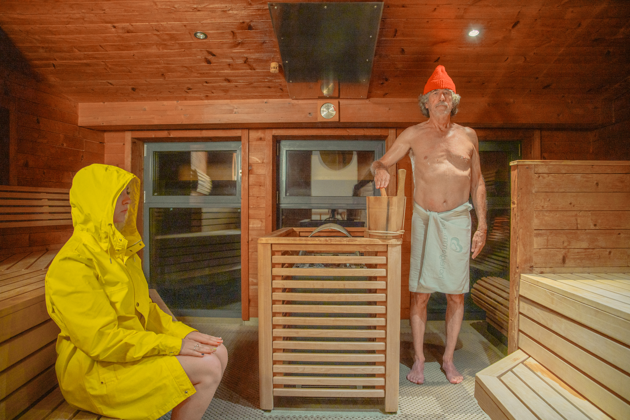 In der Sauna im Glemmtal entspannen zwei Personen, eine in gelbem Regenmantel, der andere bereit zum Saunieren.