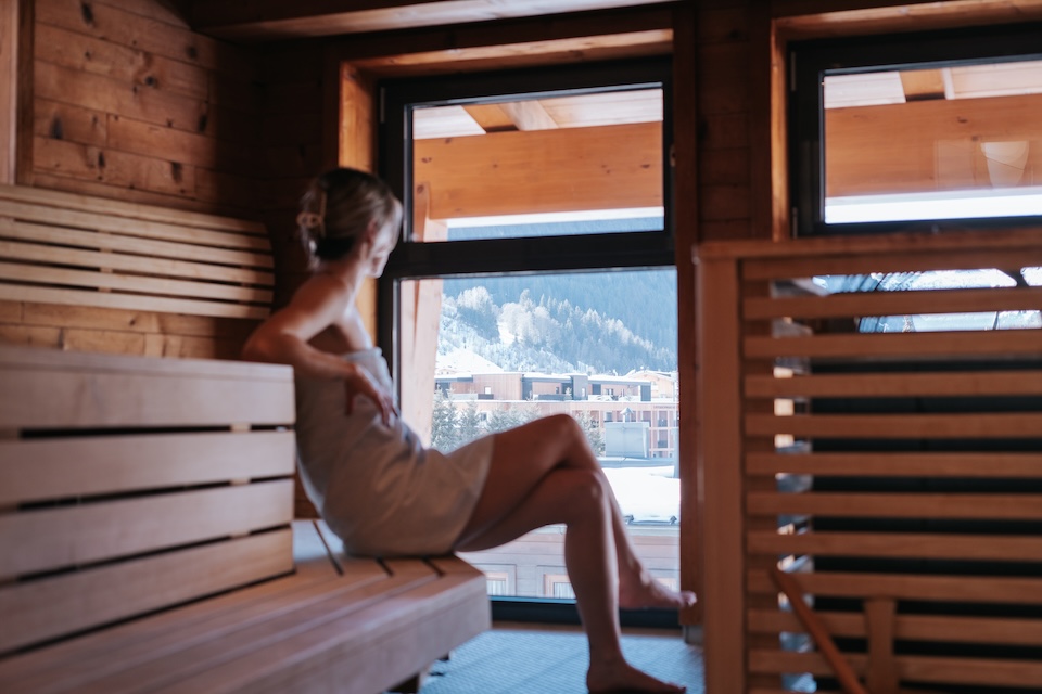 A serene spa scene at the Glemmtalerhof in Hinterglemm, featuring a woman relaxing in the sauna with a mountain view.
