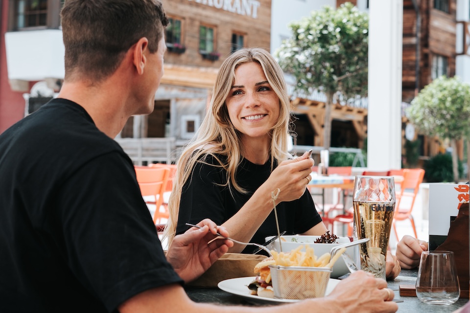 Zwei Personen genießen eine Mahlzeit im Freien, möglicherweise im Glemmtalerhof in Hinterglemm. Es ist eine freundliche Atmosphäre.