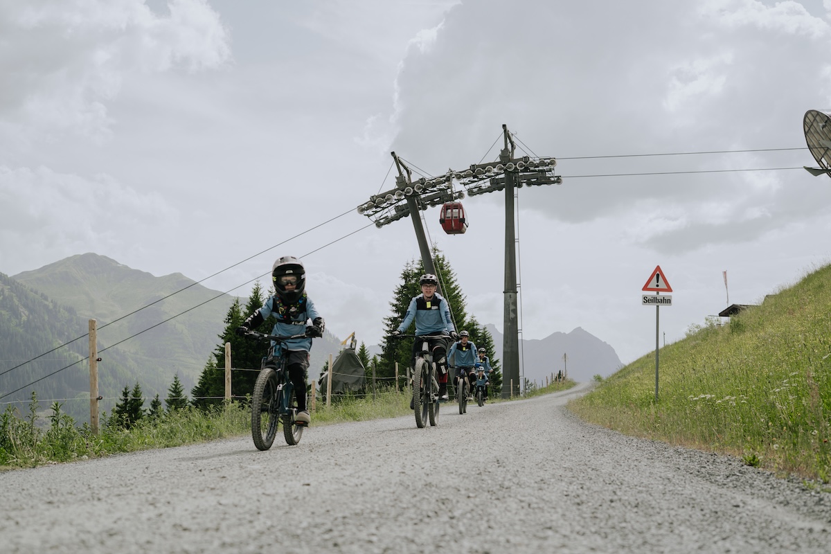 Gruppen von Radfahrern fahren im Glemmtal entlang einem Schotterweg mit Seilbahn im Hintergrund.