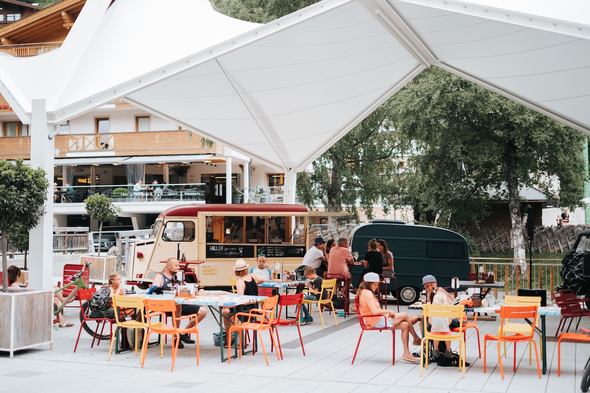 Im Glemmtal sitzen viele Gäste entspannt im Freien vor dem Glemmtalerhof und genießen verschiedene Speisen.