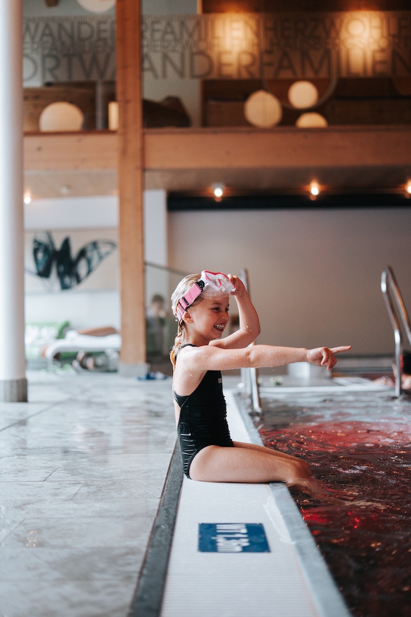 Ein Mädchen mit Schwimmbrille spielt am Rand des Beckens im Glemmtalerhof in Hinterglemm.
