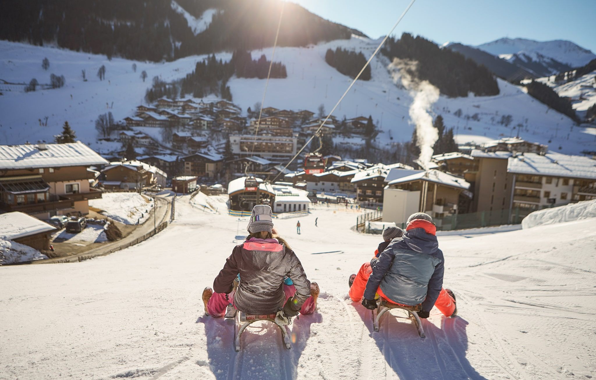 Im Glemmtal genießen Kinder das Schlittenfahren mit Blick auf die verschneiten Hütten.