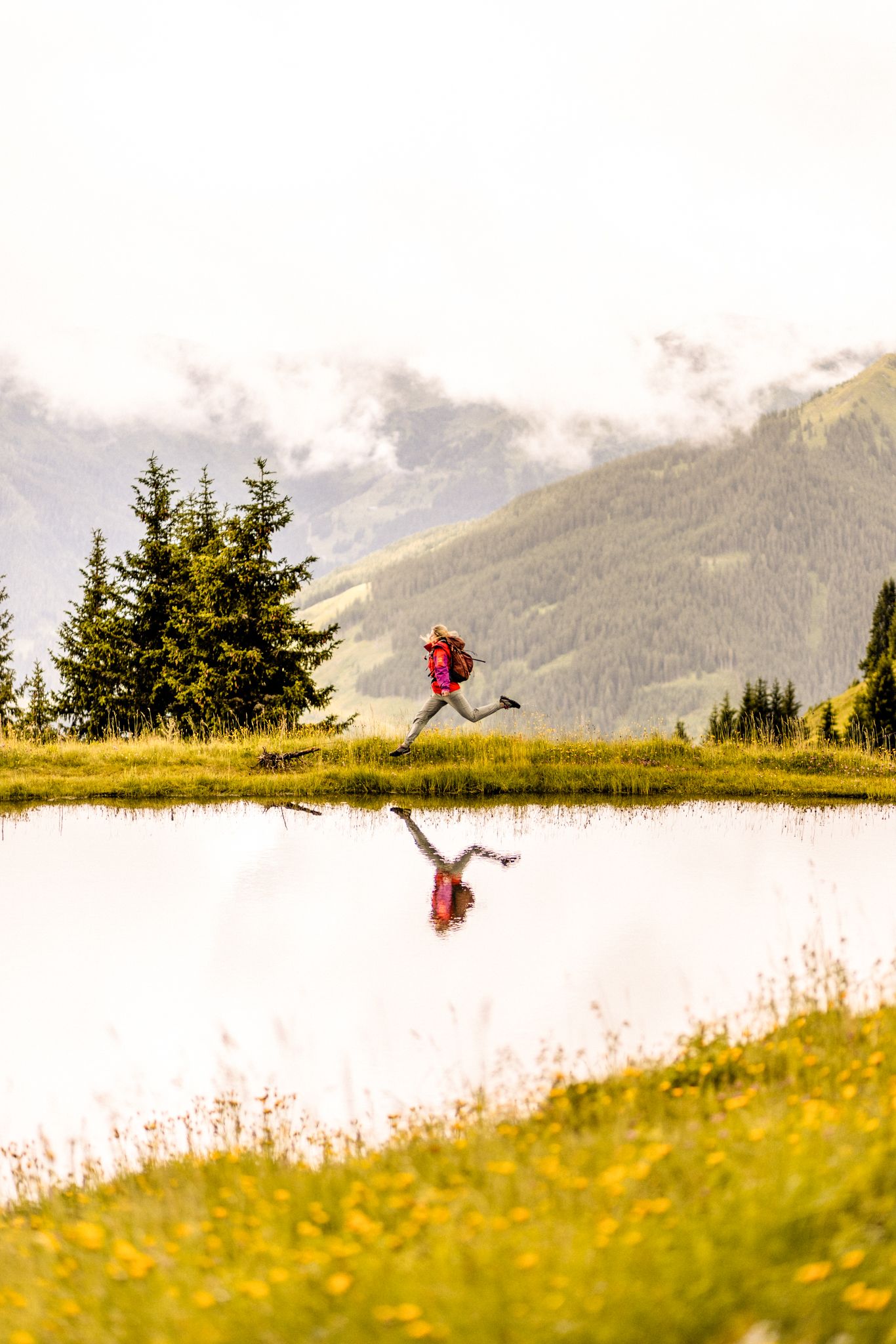 A hiker jumps over a pond in the Glemmtal with mountains in the background.