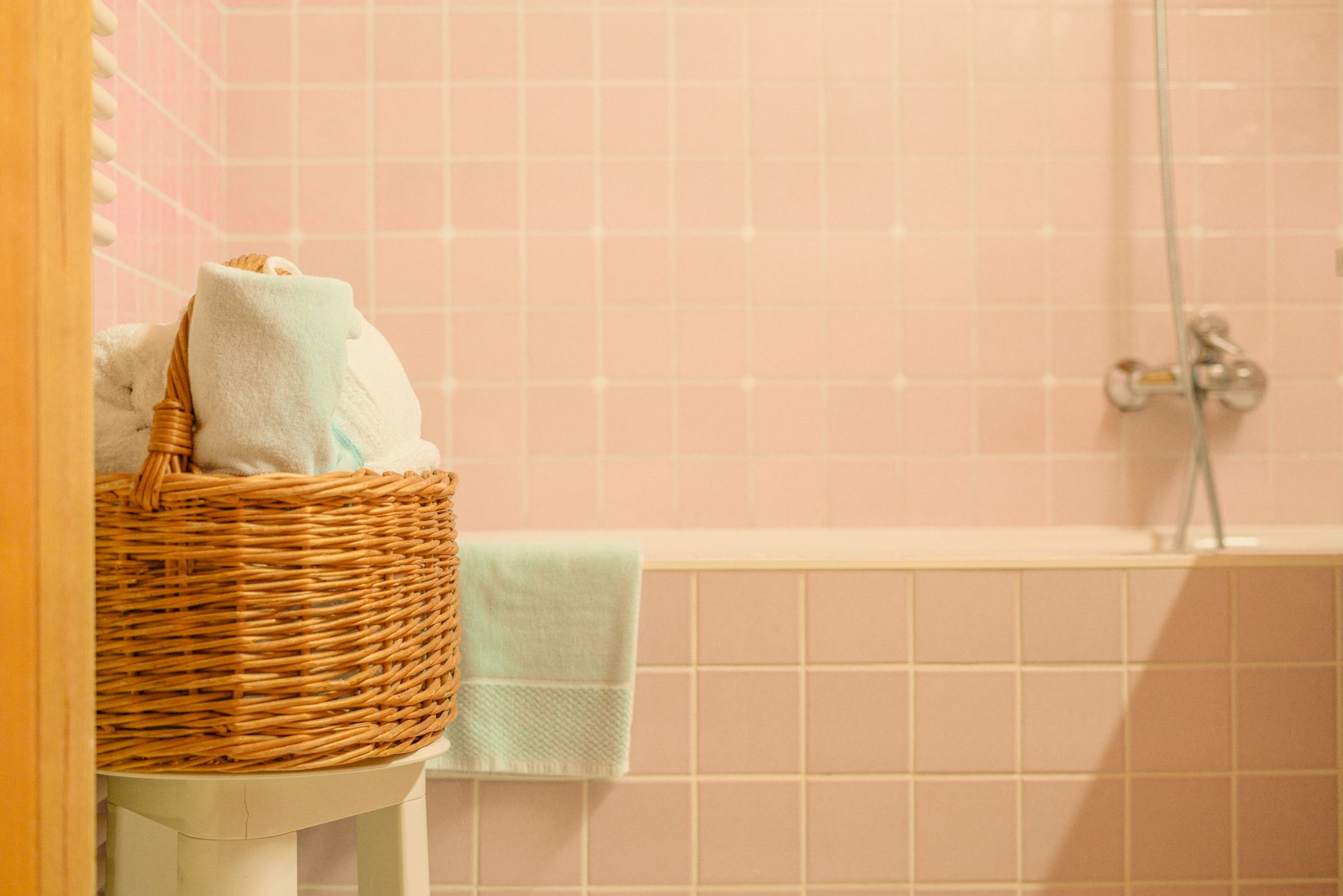 A cozy bathroom with towels in a basket and soft pink tiles.