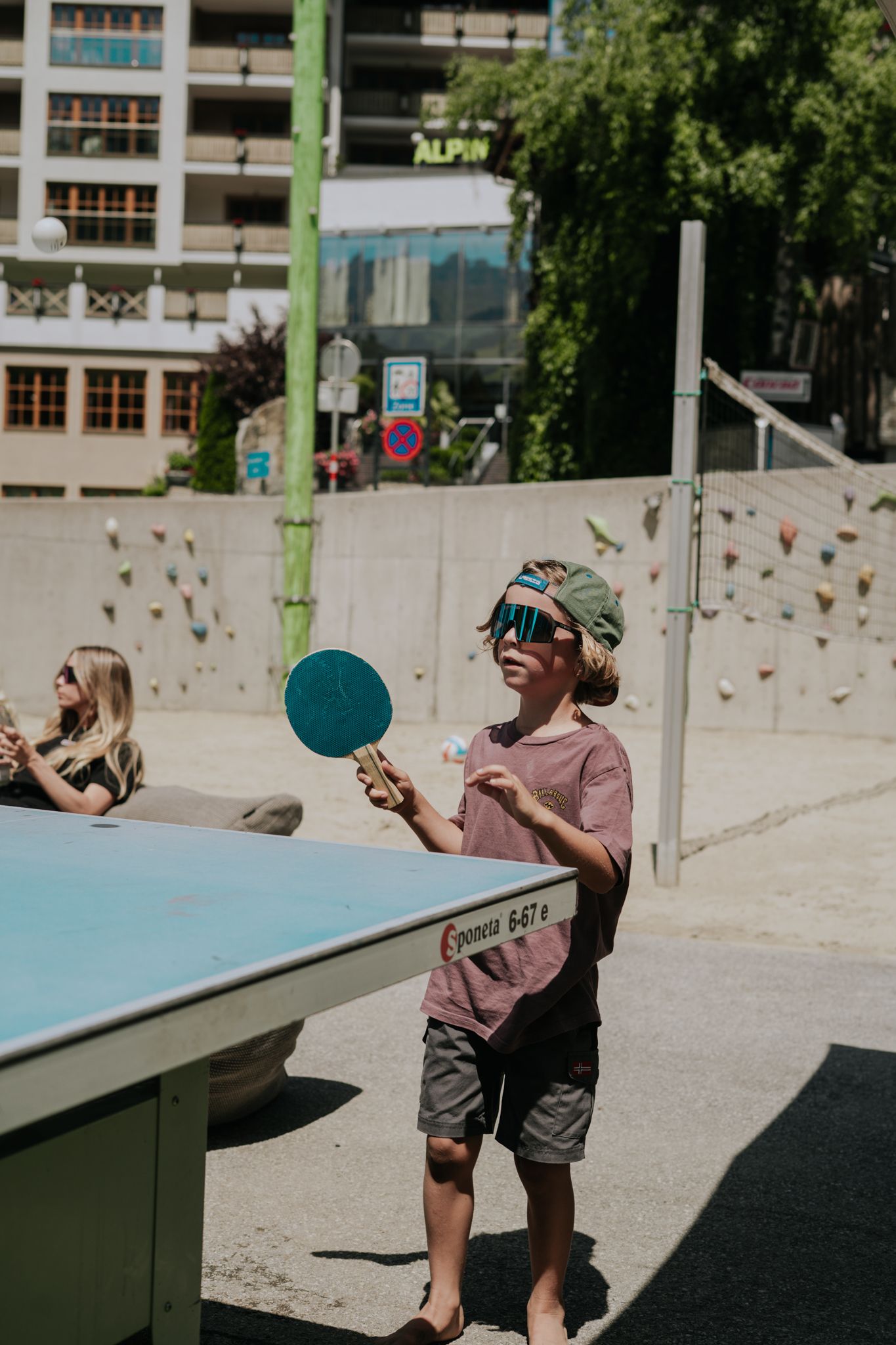 A boy plays table tennis in the Glemmtal, with the Glemmtalerhof building visible in the background
