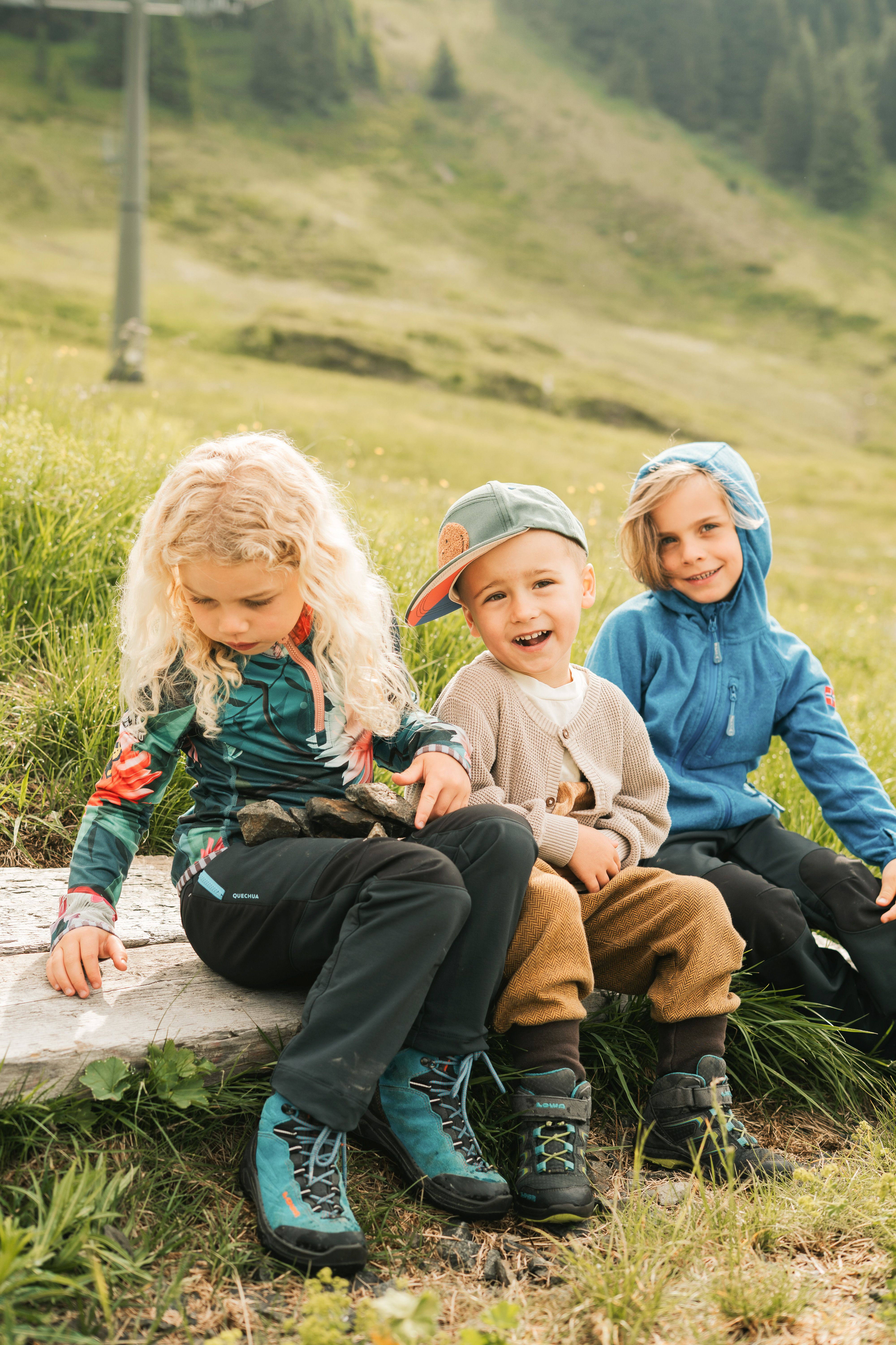 Drei Kinder im Glemmtal sitzen auf einem Baumstamm und genießen die Natur.