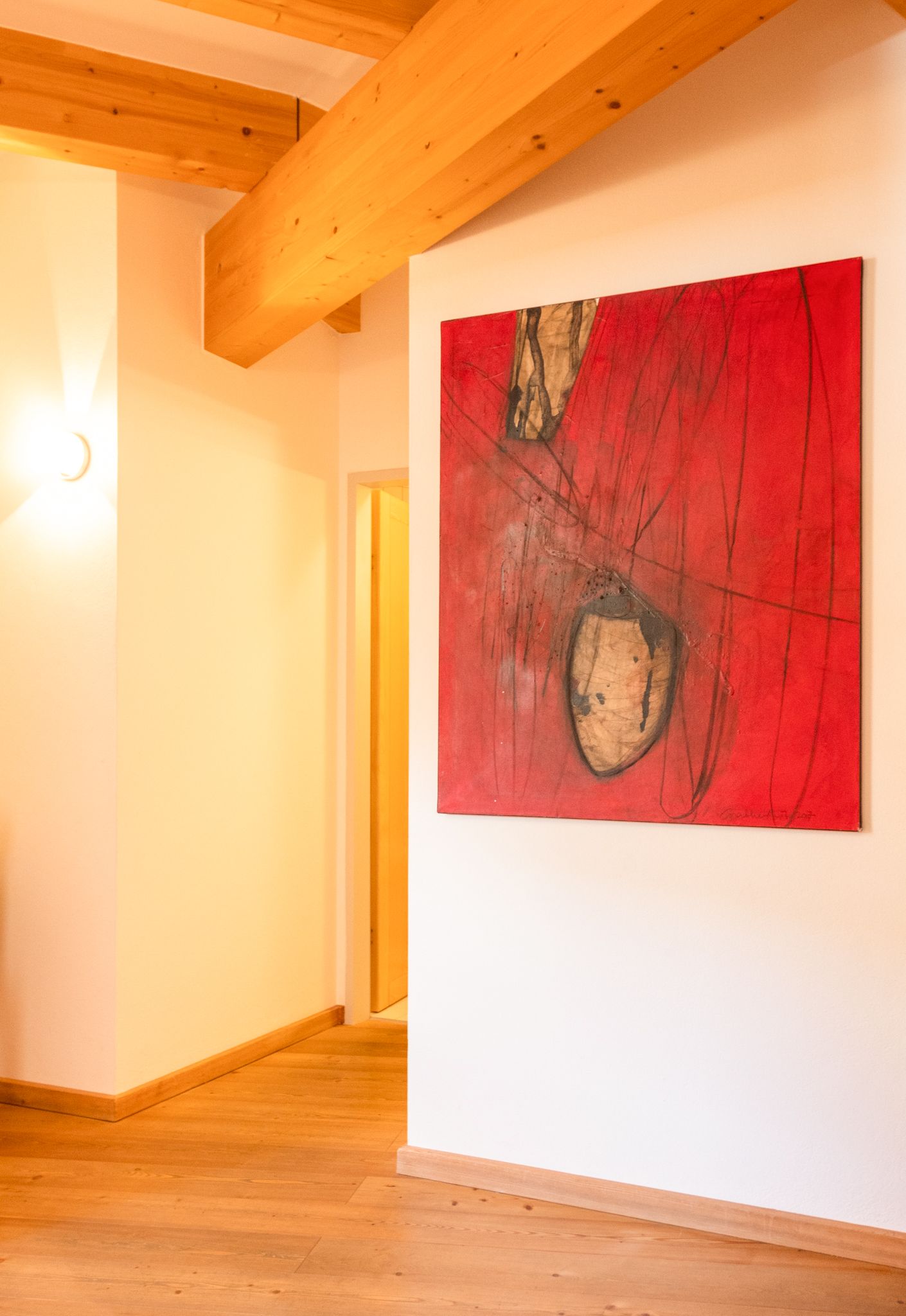 Ein rotes Gemälde an der Wand im Glemmtalerhof, warmes Holz und einladende Atmosphäre.