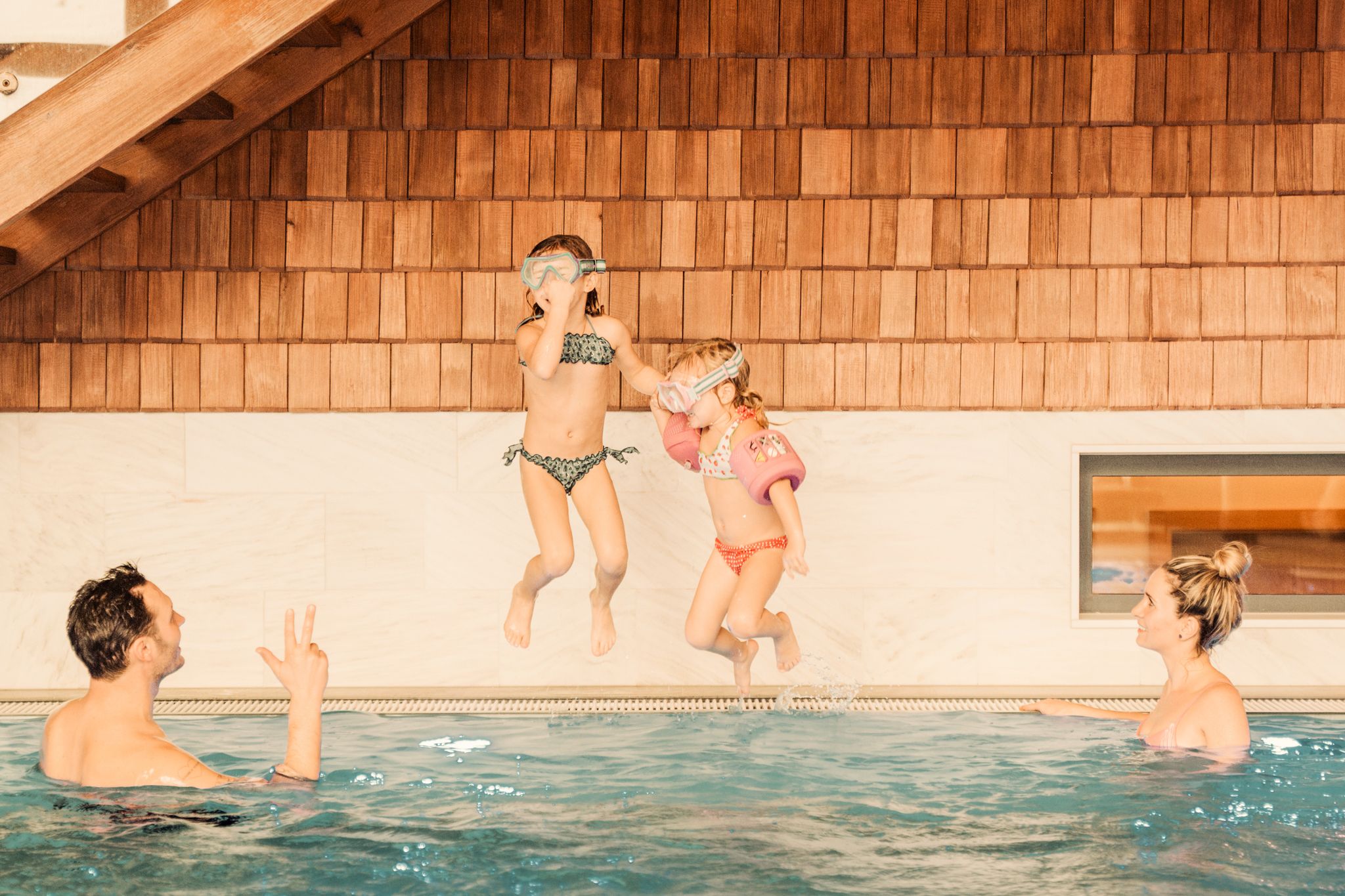 Two girls jump in the pool at Glemmtalerhof while adults watch and enjoy.