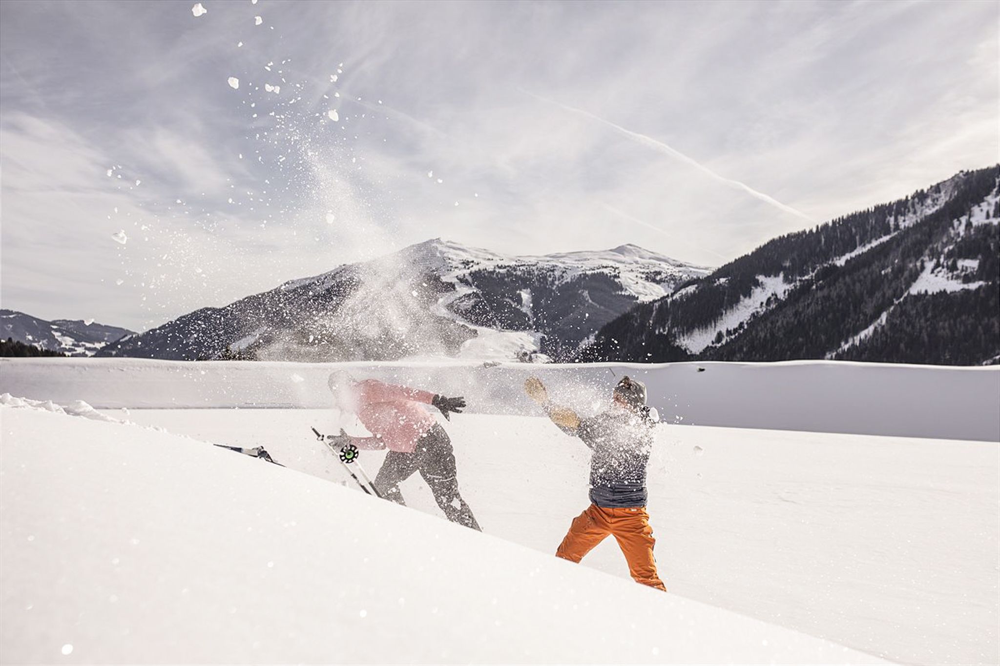 Two skiers in Glemmtal play in the snow, throwing snow at each other.