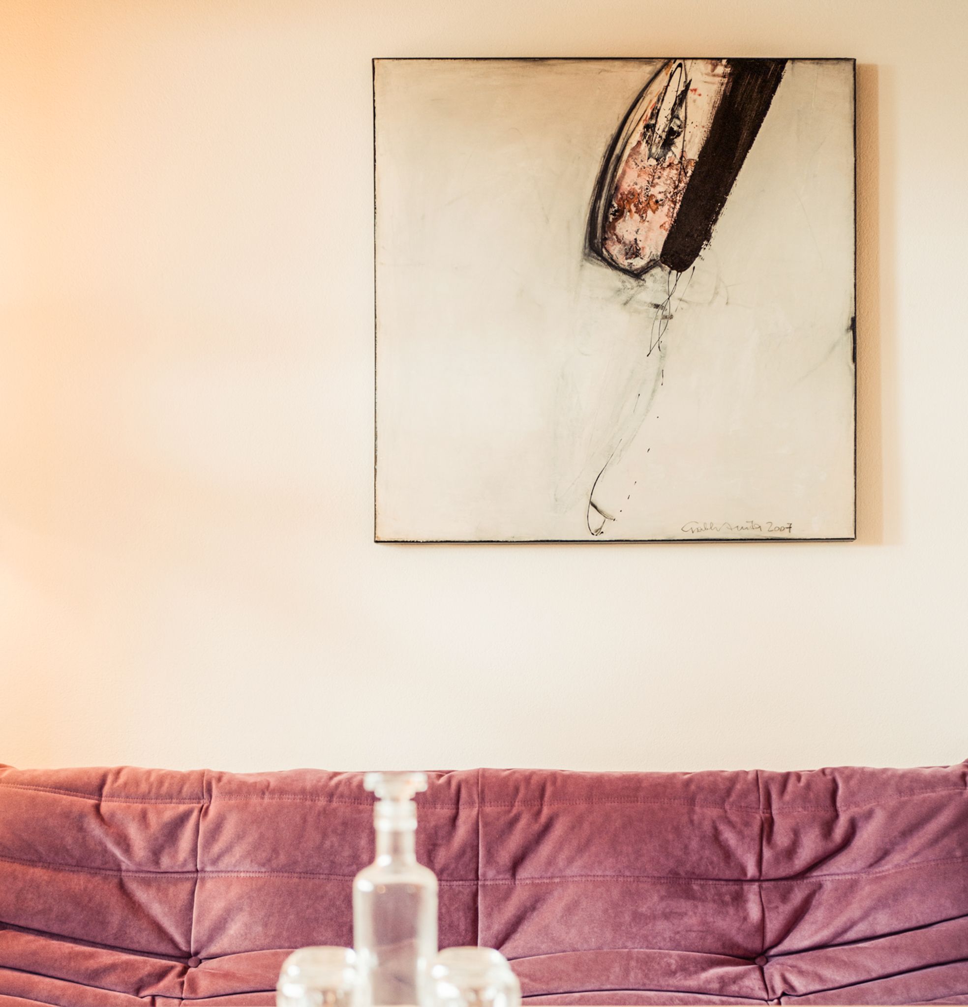Gemütliche Ecke im Glemmtalerhof, mit modernem Kunstwerk über einer lila Couch. DE