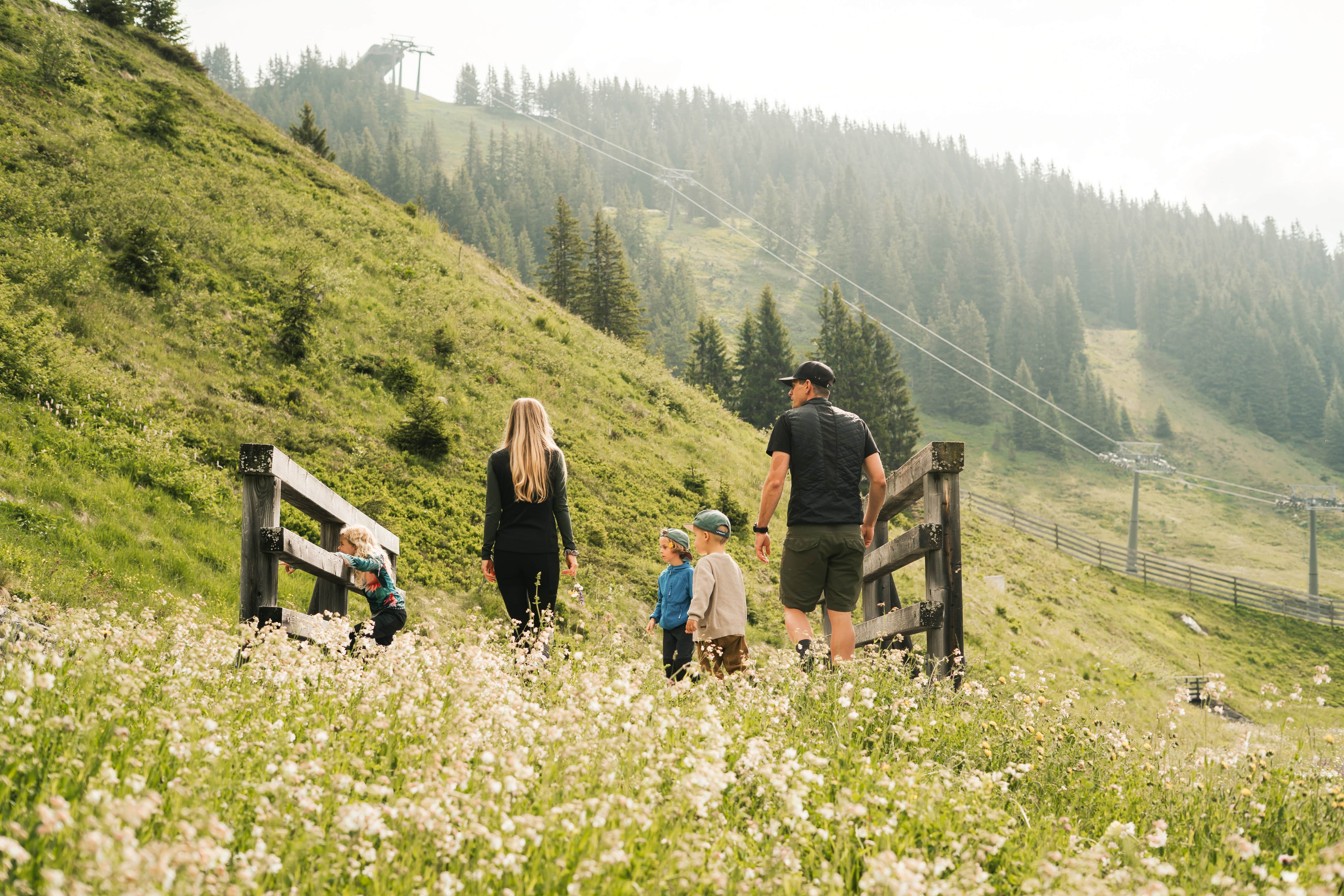 Eine Familie wandert durch blühende Wiesen im Glemmtal, mit Ausblick auf die Berge.