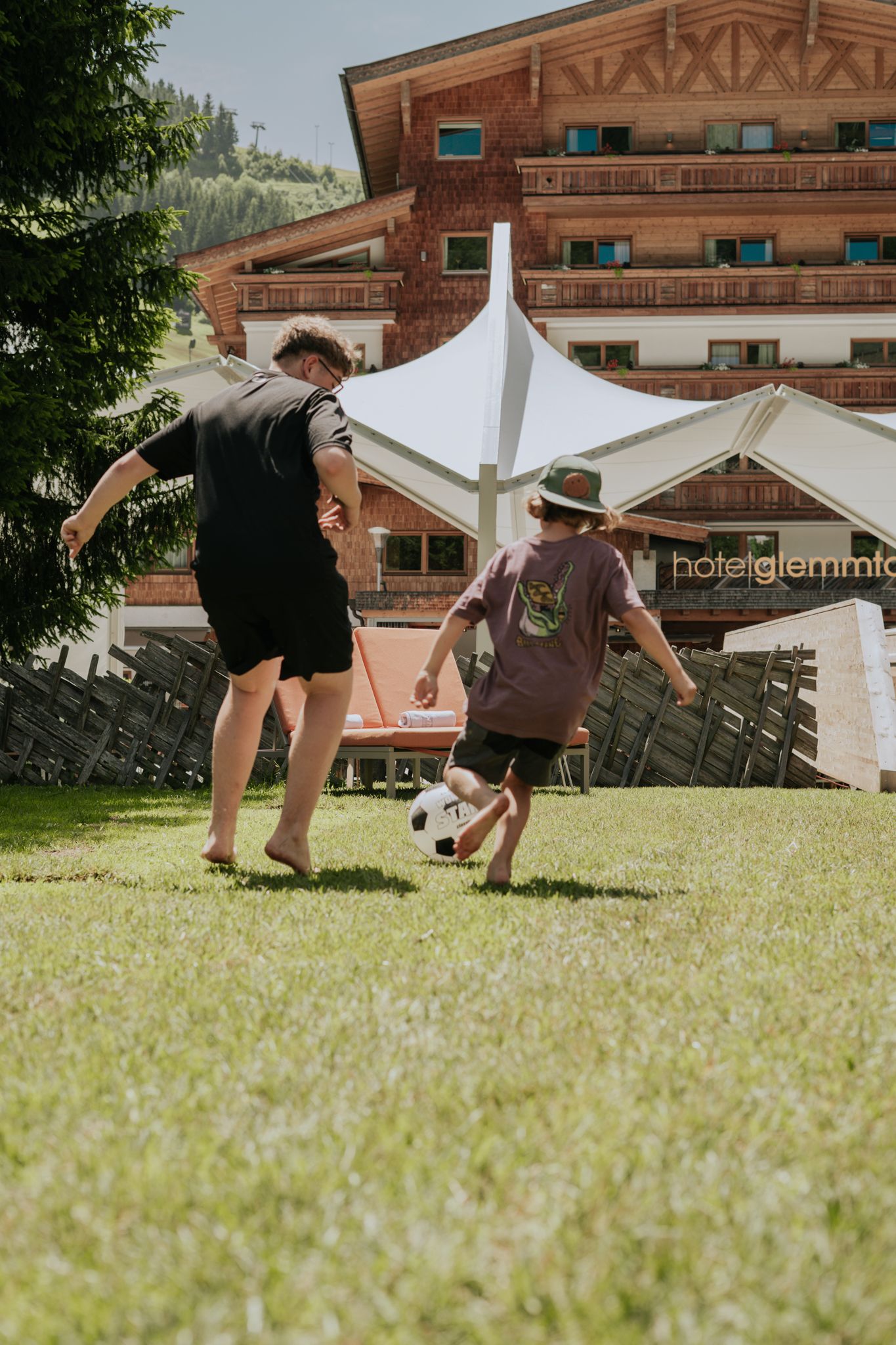 Father and son play soccer at Glemmtalerhof in Hinterglemm. It is a sunny day.