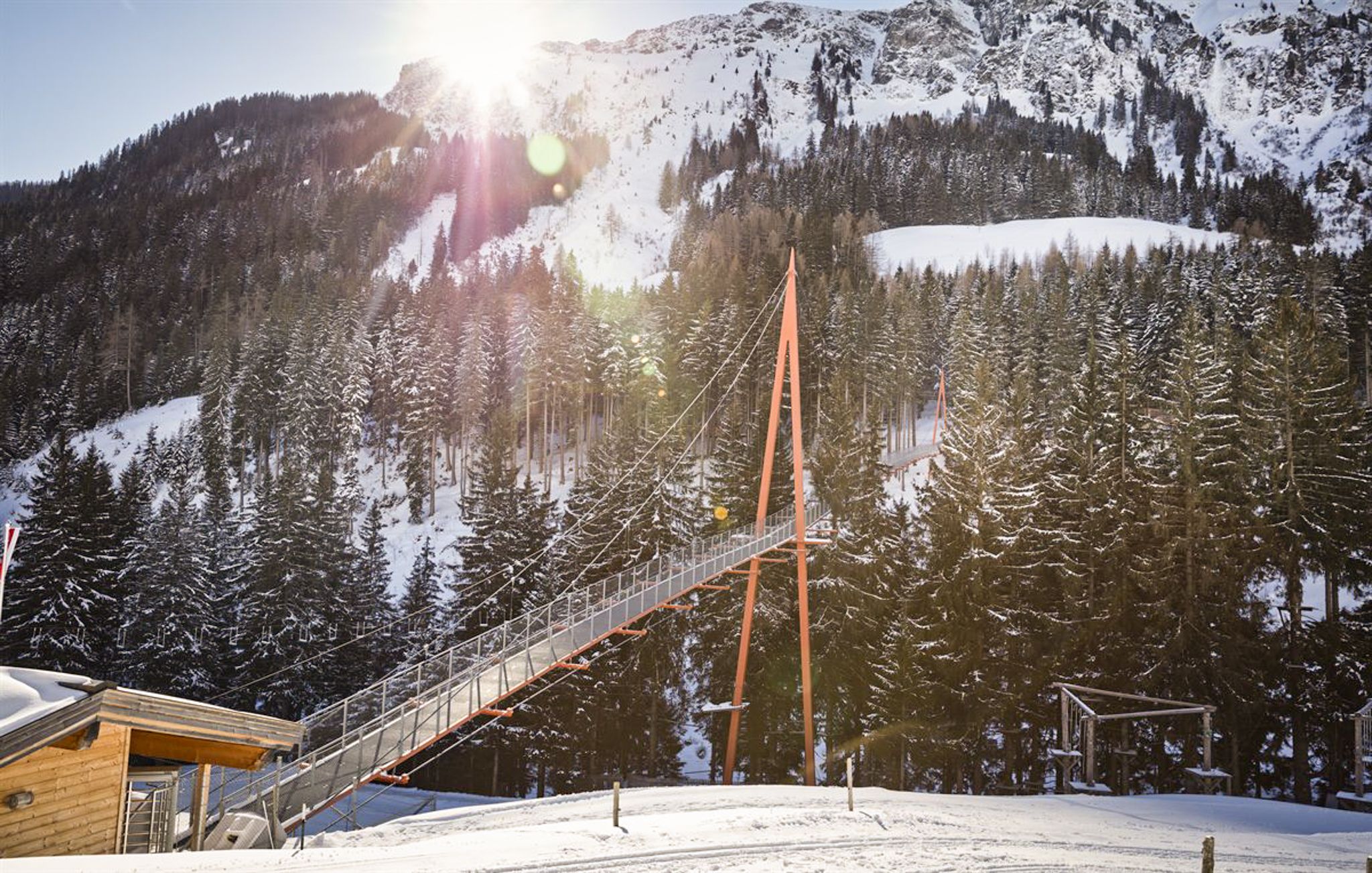 A suspension bridge in the snowy Glemmtal landscape with mountains and pine trees.