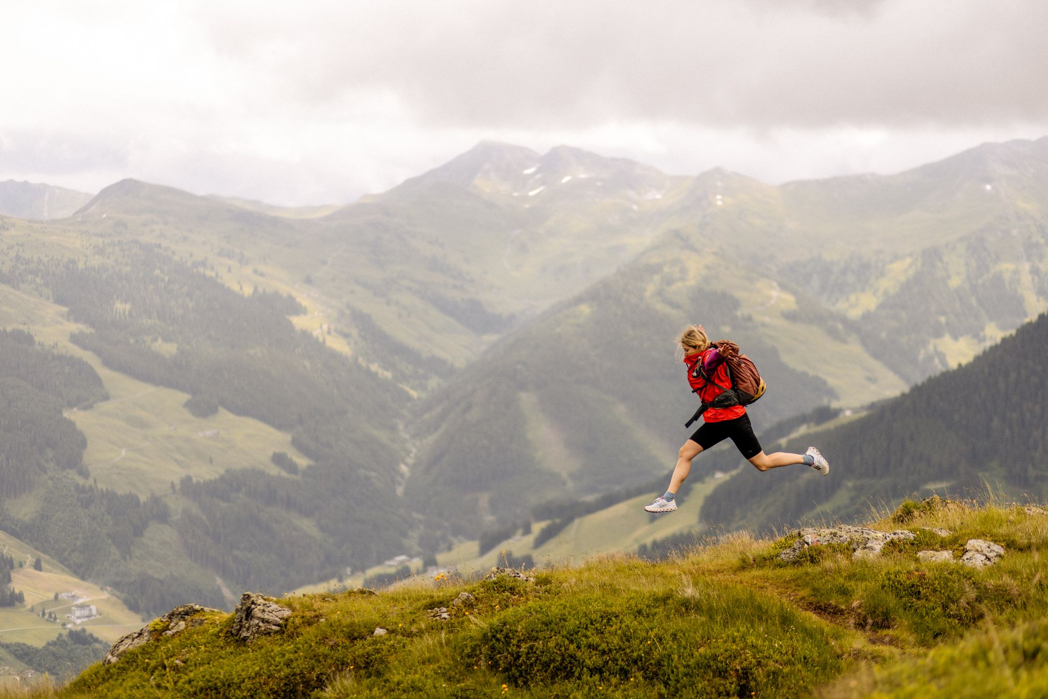 A person jumps with a backpack over a meadow in the Glemmtal mountains.