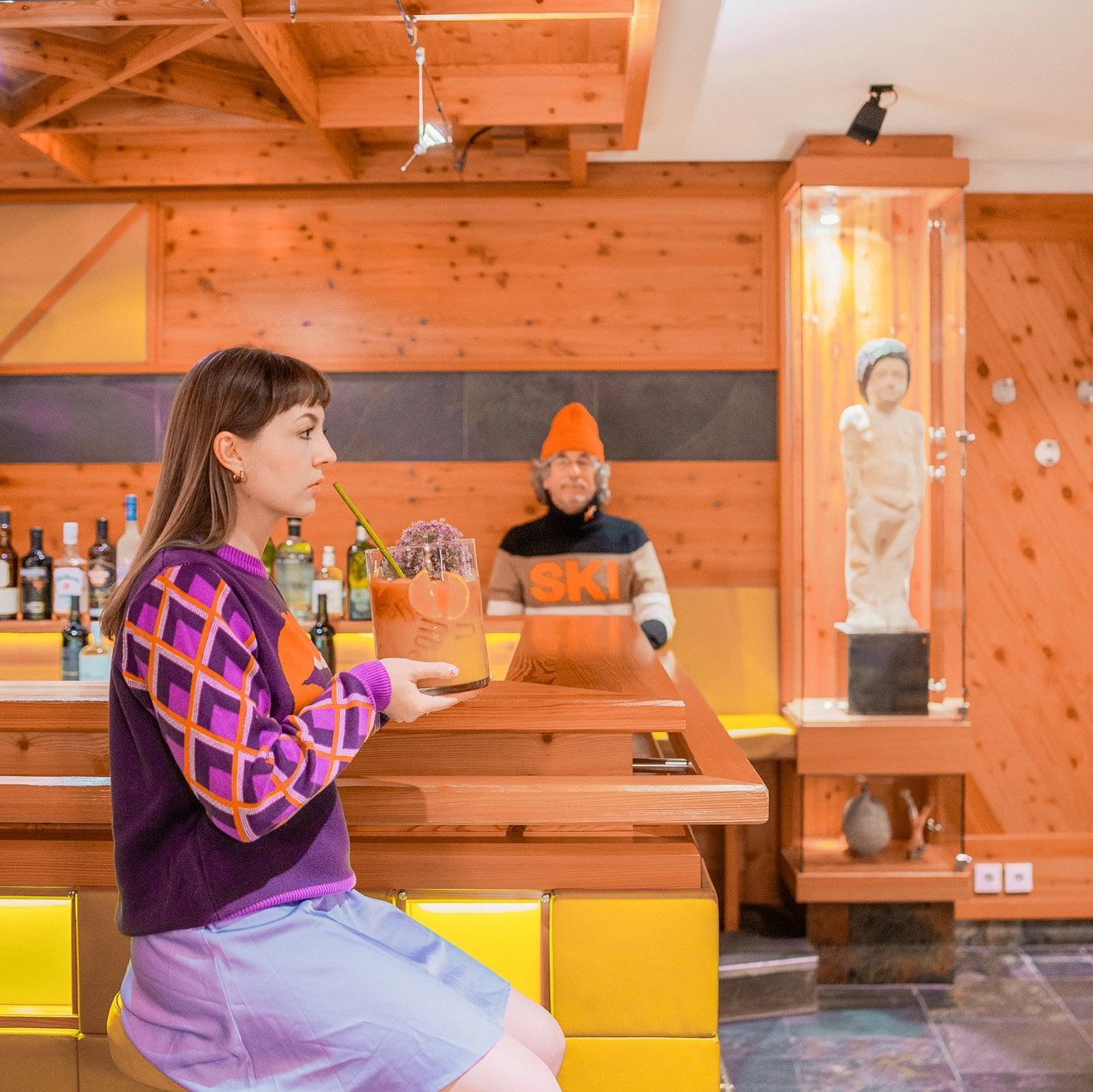 A woman sits at the bar in Glemmtalerhof holding a drink.