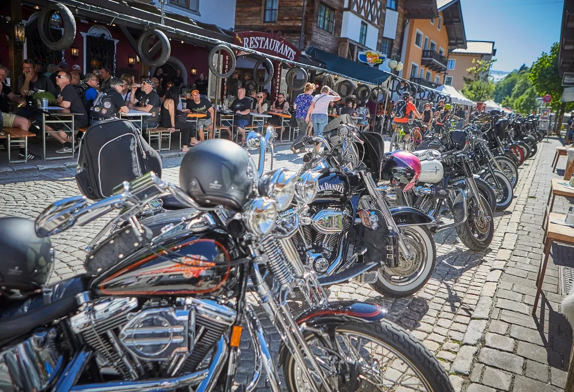 Colorful motorcycles are parked in front of the Glemmtalerhof in Hinterglemm, as guests relax outside.