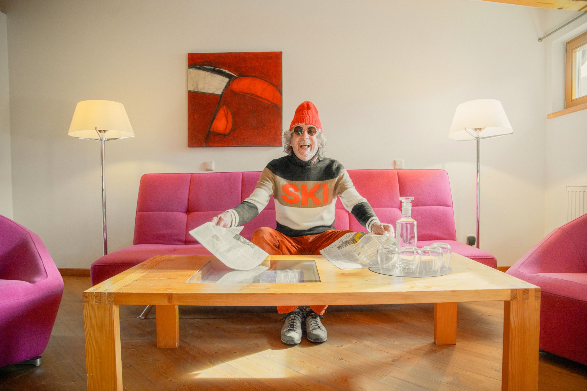 A cheerful man sits in the Glemmtalerhof, surrounded by purple sofas and getting