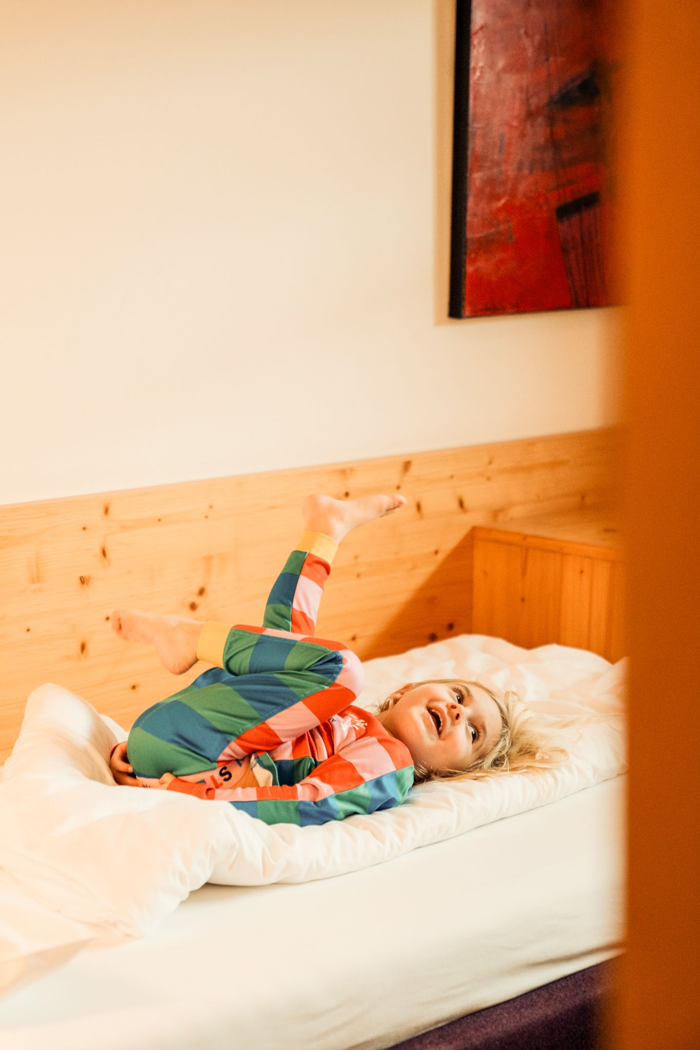 A joyful child in colorful pajamas lies in the Glemmtalerhof bed, enjoying relaxation.